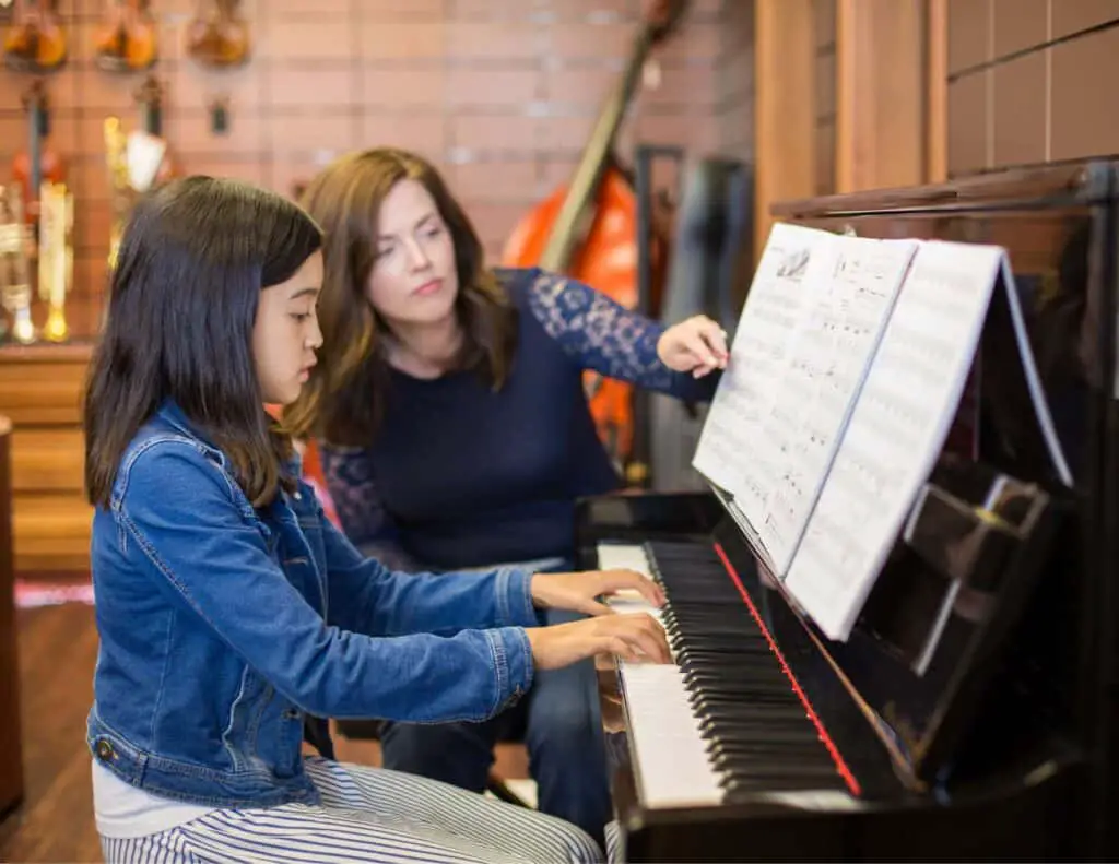 Woman teaching a girl how to play piano.