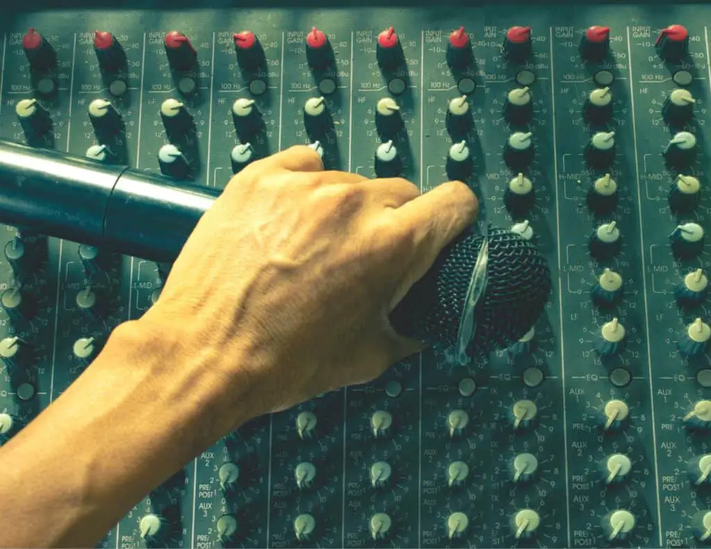 Man holding a wireless mic while adjusting a mixer.